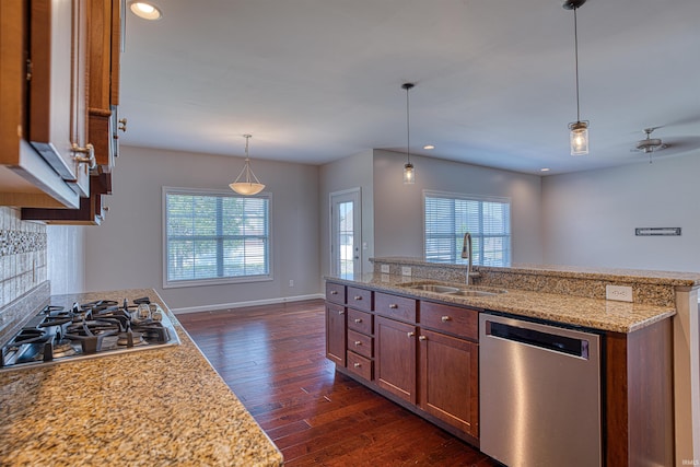 kitchen featuring pendant lighting, stainless steel appliances, sink, light stone countertops, and dark wood-type flooring