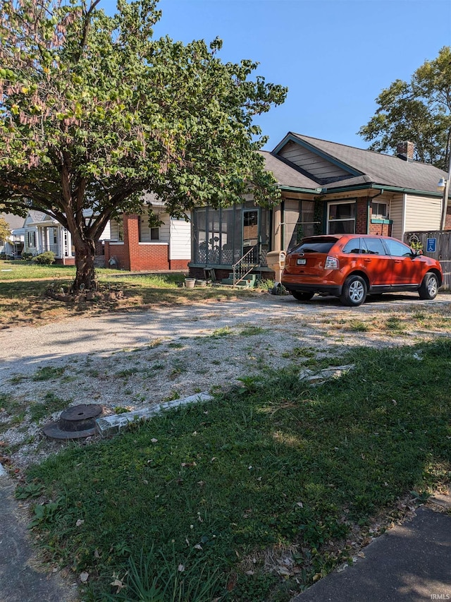 view of front of property with a sunroom, brick siding, driveway, and a front lawn