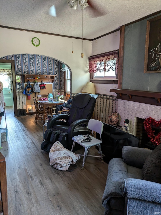 living area with a textured ceiling, ornamental molding, a fireplace, and wood finished floors