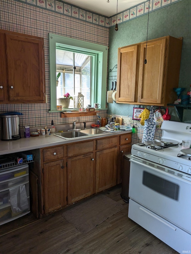 kitchen featuring brown cabinetry, dark wood-style flooring, gas range gas stove, light countertops, and a sink