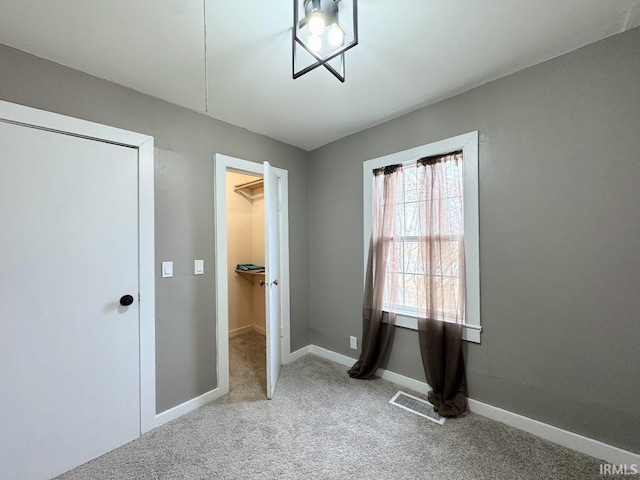 unfurnished bedroom featuring a spacious closet, carpet, visible vents, and baseboards