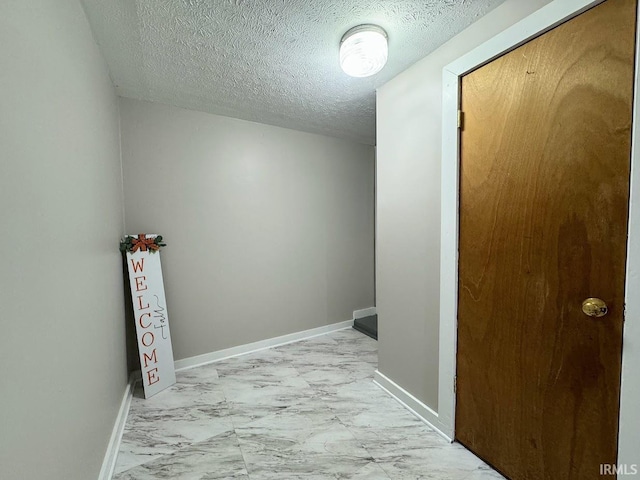 corridor featuring marble finish floor, baseboards, and a textured ceiling