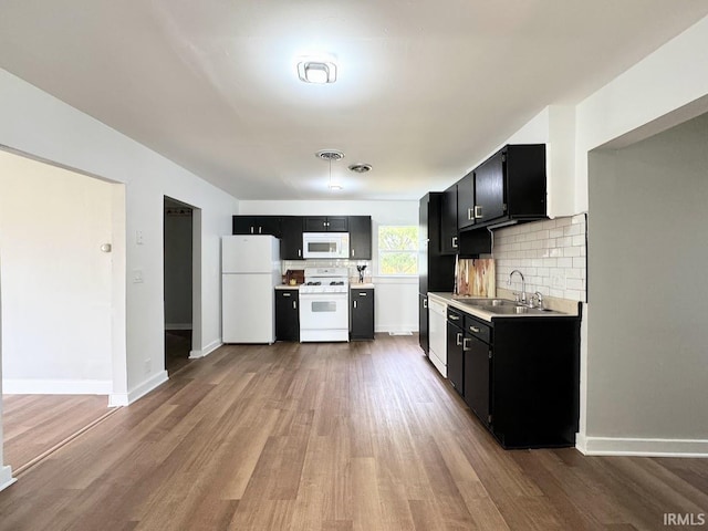 kitchen with a sink, white appliances, dark cabinets, and wood finished floors