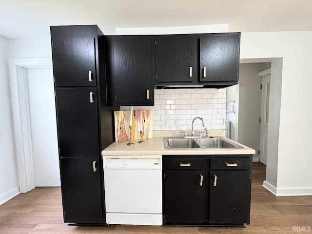 kitchen with white dishwasher, a sink, dark cabinetry, light wood-type flooring, and tasteful backsplash