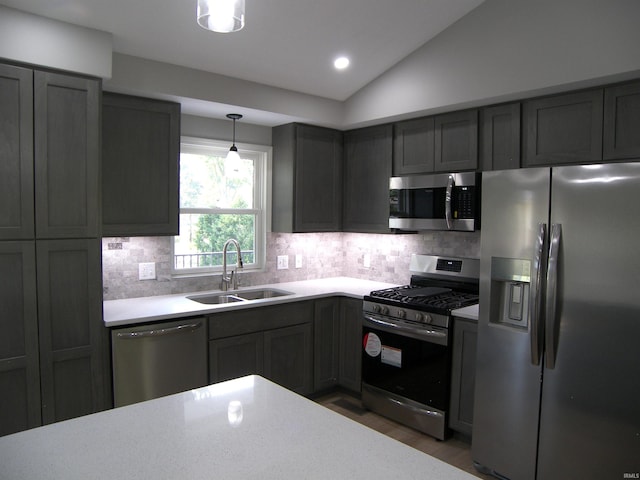 kitchen featuring stainless steel appliances, tasteful backsplash, light countertops, vaulted ceiling, and a sink