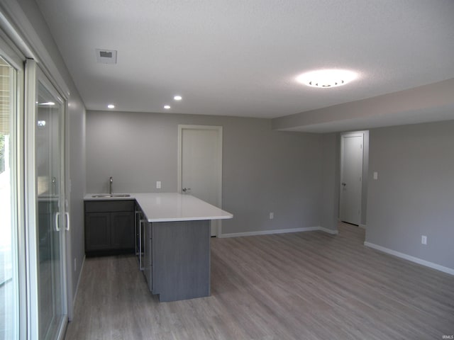 kitchen with baseboards, a peninsula, light countertops, light wood-style floors, and a sink