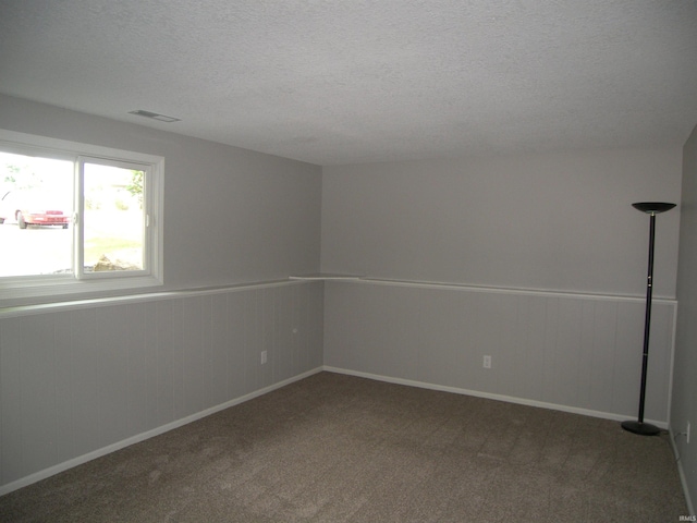 carpeted empty room featuring a wainscoted wall, visible vents, and a textured ceiling