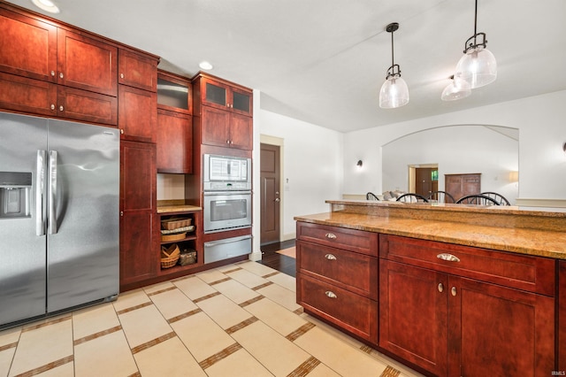 kitchen with hanging light fixtures, white microwave, stainless steel fridge, and light stone countertops