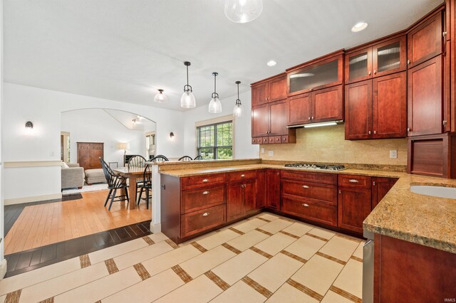 kitchen featuring backsplash, stainless steel gas stovetop, light hardwood / wood-style flooring, light stone countertops, and pendant lighting