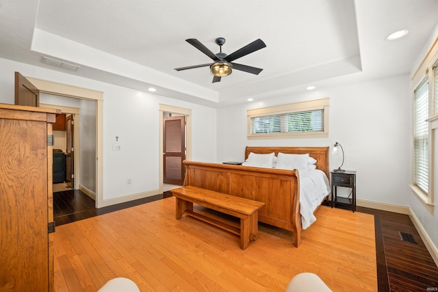 bedroom with a tray ceiling, dark hardwood / wood-style flooring, and ceiling fan