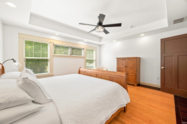 bedroom with a tray ceiling, ceiling fan, and light hardwood / wood-style flooring