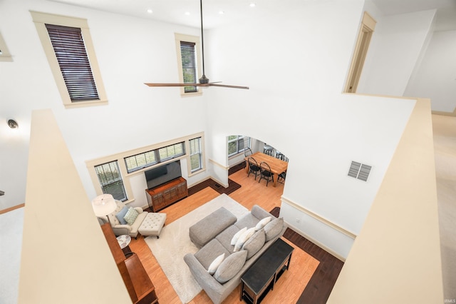 living room featuring a high ceiling, ceiling fan, and light hardwood / wood-style floors