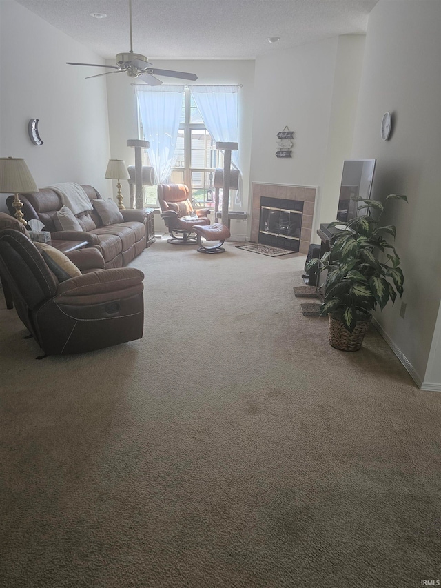 carpeted living room featuring ceiling fan, a tiled fireplace, and a textured ceiling