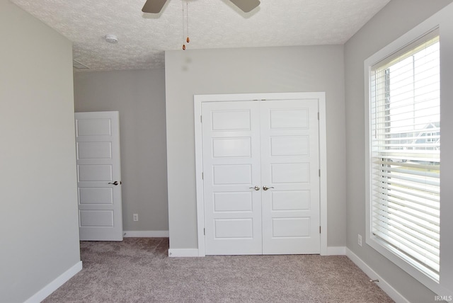 unfurnished bedroom with ceiling fan, a closet, light colored carpet, and a textured ceiling