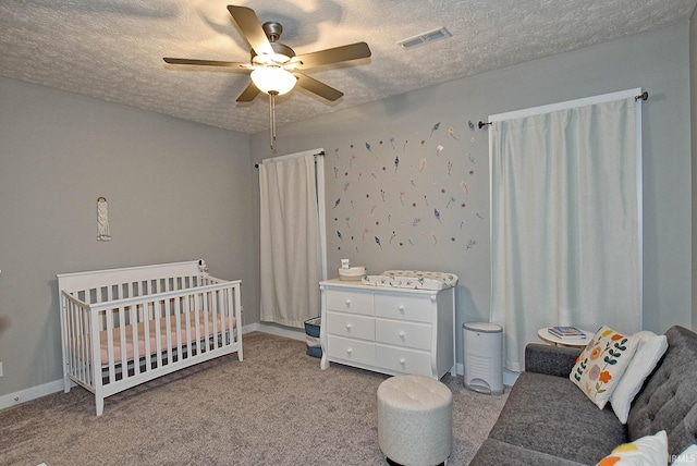 bedroom with ceiling fan, a nursery area, a textured ceiling, and light carpet