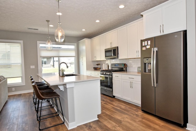 kitchen with appliances with stainless steel finishes, a center island with sink, white cabinetry, and sink