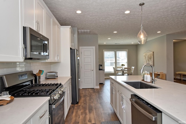 kitchen with pendant lighting, dark wood-type flooring, white cabinets, sink, and appliances with stainless steel finishes