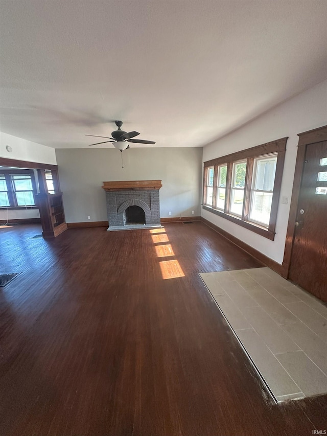 unfurnished living room with dark wood-type flooring, ceiling fan, and a brick fireplace