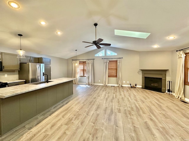 interior space with light wood-type flooring, light stone counters, sink, stainless steel fridge, and ceiling fan