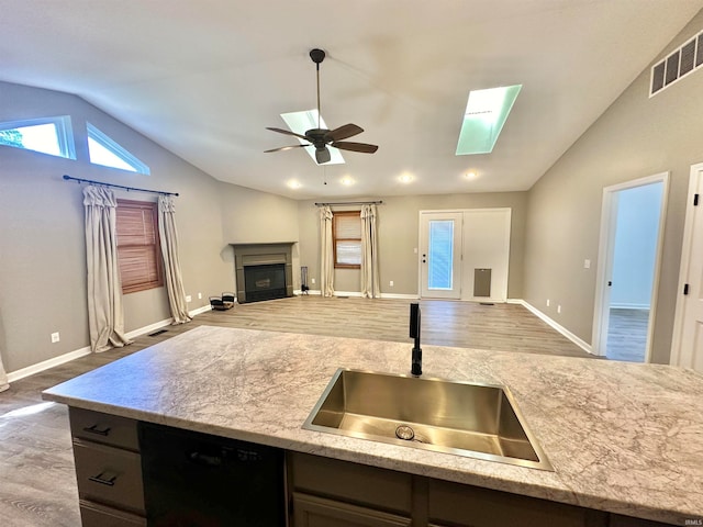 kitchen featuring lofted ceiling with skylight, black dishwasher, wood-type flooring, sink, and ceiling fan