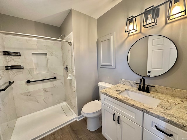 bathroom with vanity, toilet, hardwood / wood-style flooring, and tiled shower