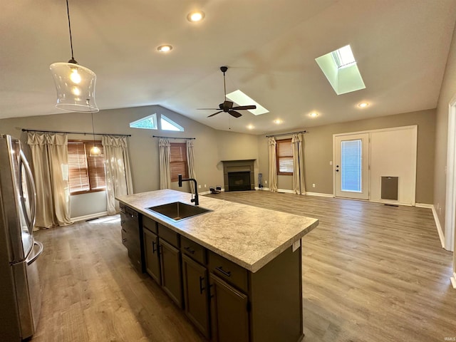 kitchen featuring vaulted ceiling with skylight, stainless steel fridge, light hardwood / wood-style flooring, ceiling fan, and a center island with sink