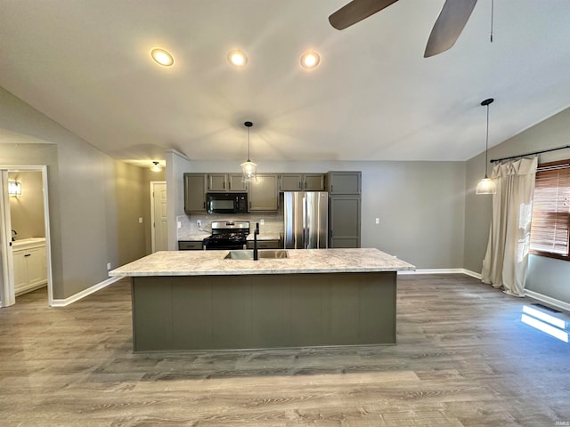 kitchen with light stone counters, sink, an island with sink, ceiling fan, and appliances with stainless steel finishes