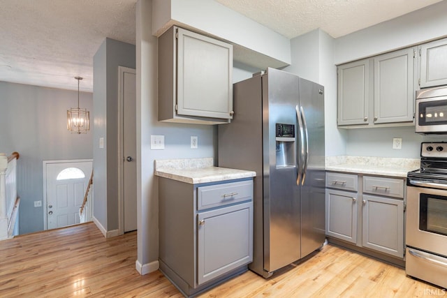 kitchen featuring a textured ceiling, light hardwood / wood-style floors, stainless steel appliances, gray cabinets, and a chandelier