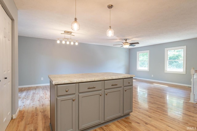 kitchen with gray cabinetry, light hardwood / wood-style flooring, ceiling fan, a kitchen island, and pendant lighting