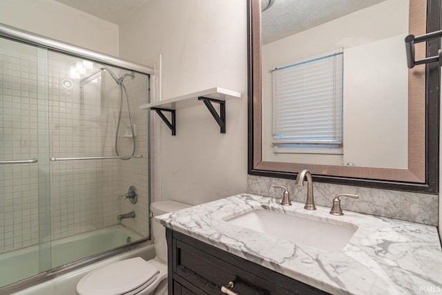 full bathroom featuring shower / bath combination with glass door, vanity, toilet, and a textured ceiling