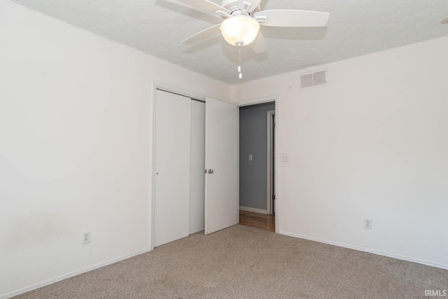 unfurnished bedroom with light carpet, a textured ceiling, ceiling fan, and a closet