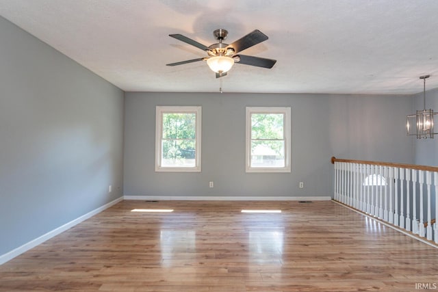 unfurnished room with ceiling fan with notable chandelier, a textured ceiling, and light hardwood / wood-style floors