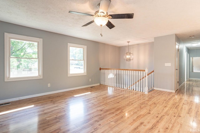 unfurnished room with a wealth of natural light, a textured ceiling, ceiling fan with notable chandelier, and light hardwood / wood-style floors