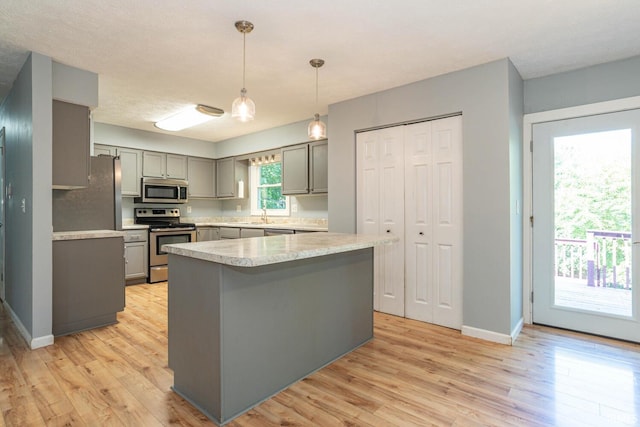 kitchen with light wood-type flooring, sink, hanging light fixtures, appliances with stainless steel finishes, and gray cabinetry