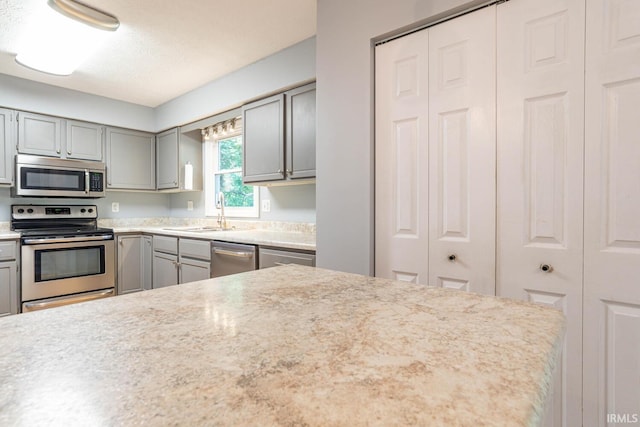 kitchen featuring a textured ceiling, sink, stainless steel appliances, and gray cabinetry