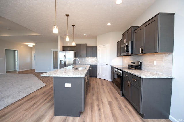 kitchen featuring a center island with sink, decorative light fixtures, light wood-type flooring, appliances with stainless steel finishes, and tasteful backsplash