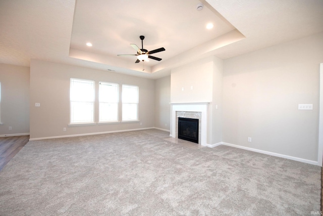 unfurnished living room with a premium fireplace, ceiling fan, light colored carpet, and a raised ceiling