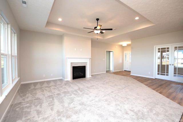 unfurnished living room featuring french doors, a tiled fireplace, a raised ceiling, and light hardwood / wood-style flooring