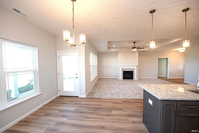 kitchen featuring light stone counters, light hardwood / wood-style flooring, hanging light fixtures, and a healthy amount of sunlight