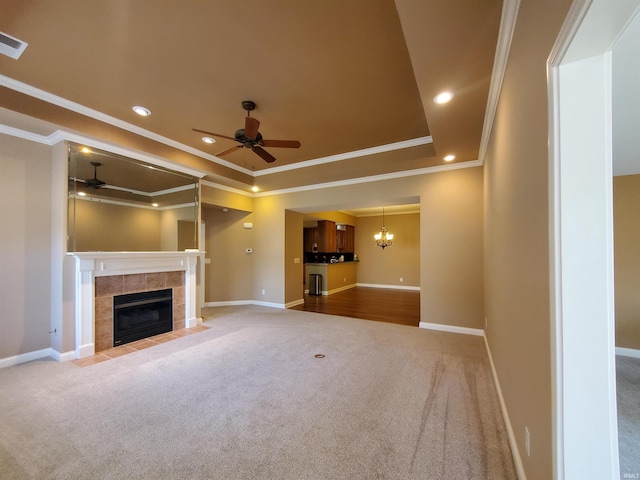 unfurnished living room with ceiling fan with notable chandelier, a fireplace, carpet, and a raised ceiling