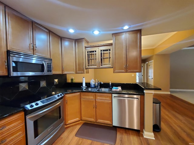 kitchen featuring appliances with stainless steel finishes, kitchen peninsula, light wood-type flooring, ornamental molding, and sink