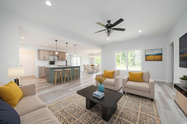 living room with ceiling fan, sink, and light wood-type flooring