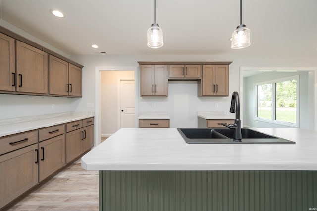 kitchen featuring light hardwood / wood-style flooring, a center island with sink, sink, and hanging light fixtures