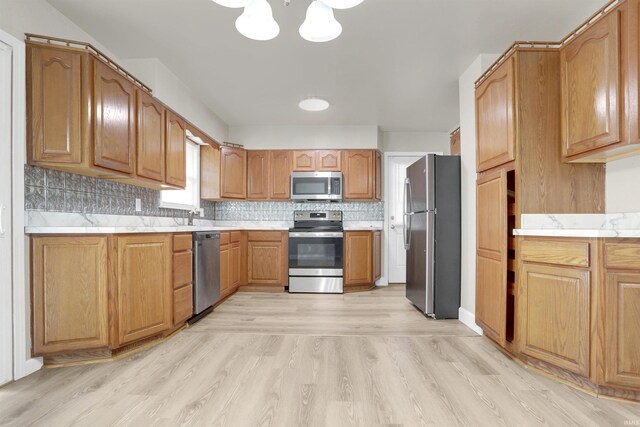 kitchen featuring appliances with stainless steel finishes, sink, tasteful backsplash, and light hardwood / wood-style flooring