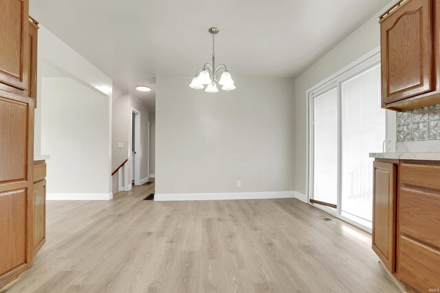 unfurnished dining area with an inviting chandelier and light hardwood / wood-style floors