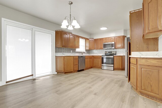 kitchen featuring light wood-type flooring, stainless steel appliances, a chandelier, pendant lighting, and tasteful backsplash