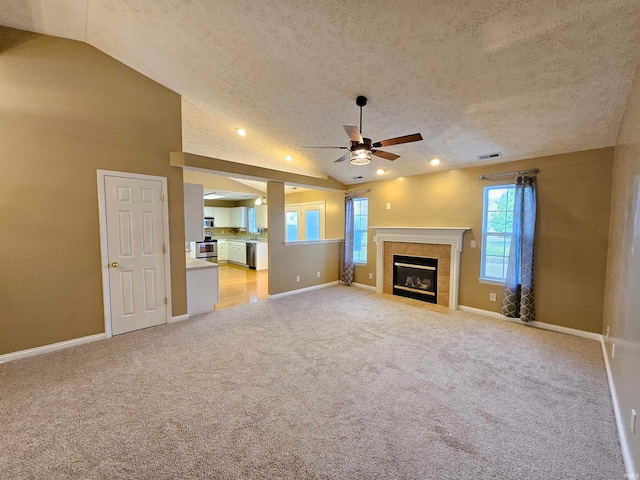 unfurnished living room featuring light colored carpet, ceiling fan, a tiled fireplace, and vaulted ceiling