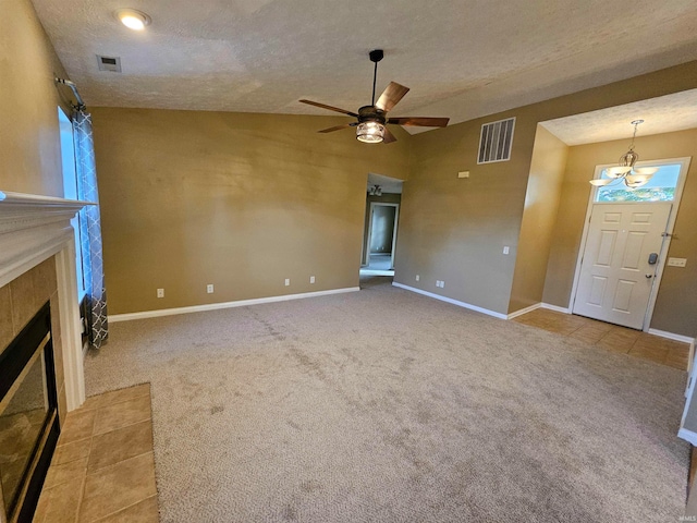 unfurnished living room with light carpet, a tiled fireplace, ceiling fan with notable chandelier, a textured ceiling, and lofted ceiling