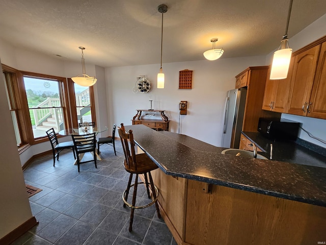 kitchen with sink, stainless steel fridge, a breakfast bar area, pendant lighting, and a textured ceiling