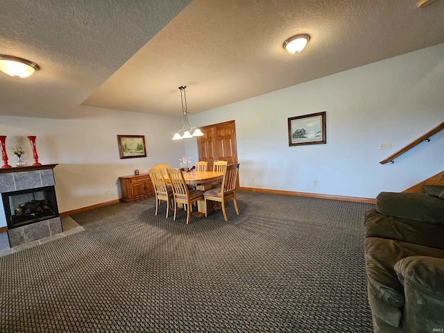 carpeted dining area with a textured ceiling, a notable chandelier, and a tile fireplace